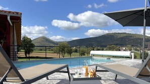 Un espace aménagé au bord de la piscine, avec des chaises longues, un foyer et une vue sur un paysage montagneux.