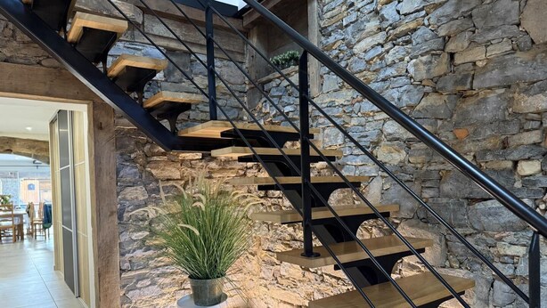 Un escalier moderne avec des marches en bois et des rampes en métal noir, menant à un mur de pierre.
