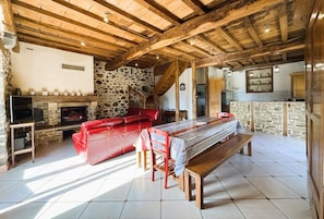 Um interior rústico com lareira de pedra, sofá de couro vermelho, mesa de jantar de madeira e área de cozinha.