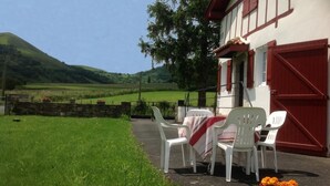 A building with a red door and white walls, a table with chairs, and a grassy area with flowers. - Caricaburia - Juxue - Gîte (JUXUE)