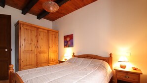 A bedroom with a wooden bed, two bedside tables with lamps, a wooden wardrobe, and a painting on the wall. - Caricaburia - Juxue - Gîte (JUXUE)
