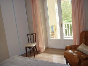 A room with a wooden floor, a brown leather sofa, a wooden chair, and a window with a view of a balcony.