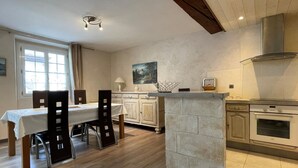 Une cuisine équipée d’une table à manger, de chaises, de placards, d’une cuisinière et d’un tableau accroché au mur.
