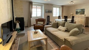 Un salon chaleureux avec une cheminée, un canapé, une table basse et un coin repas comprenant des chaises et une table.