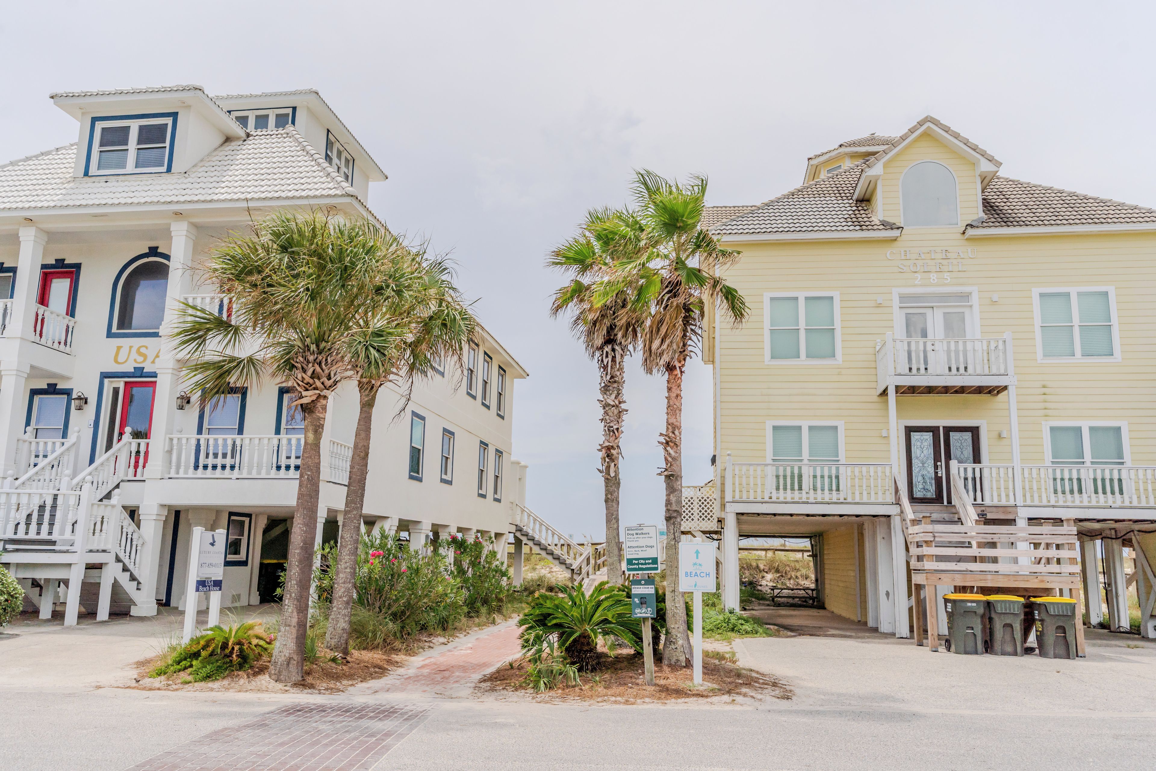 A beachfront property with a beach house sign, palm trees, and a sign indicating beach access.