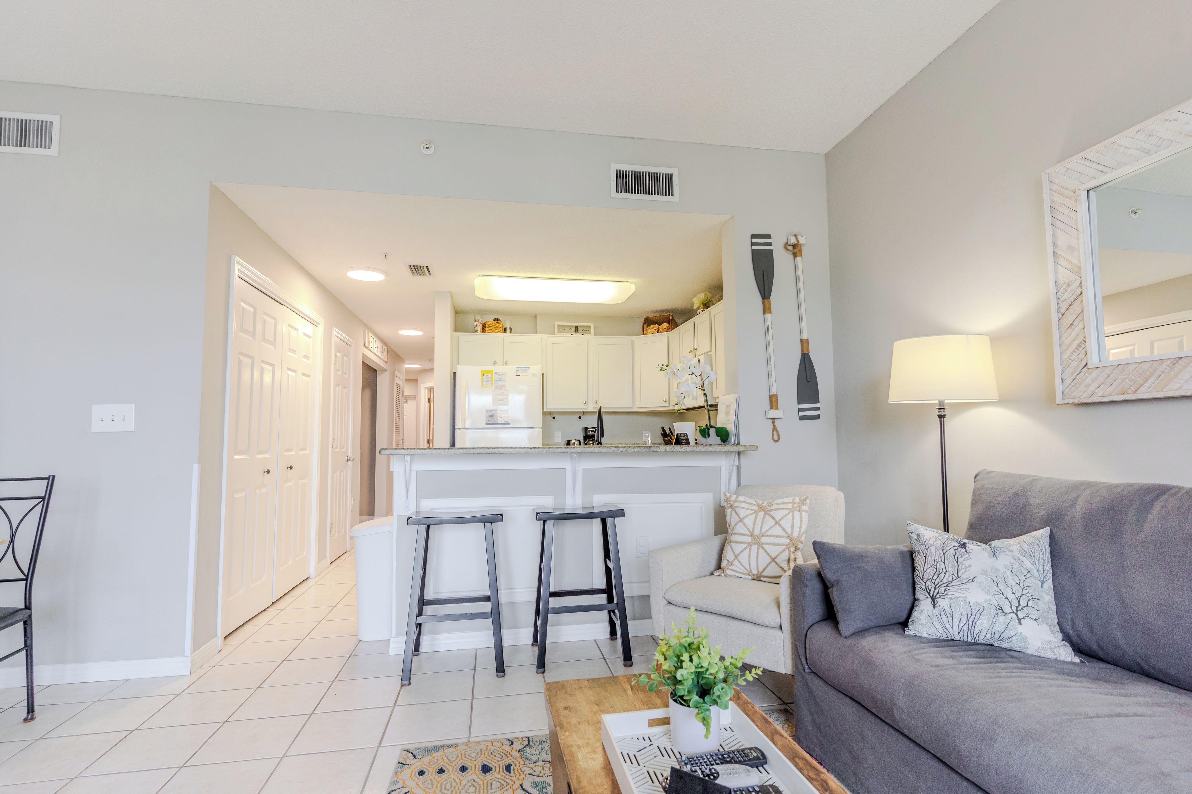A modern living room with a grey sofa, a coffee table with remote controls, and a kitchen area in the background.
