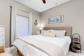 A bedroom with a bed, a nightstand, a wall-mounted lamp, a ceiling fan, a window with blinds, and a wall decoration.