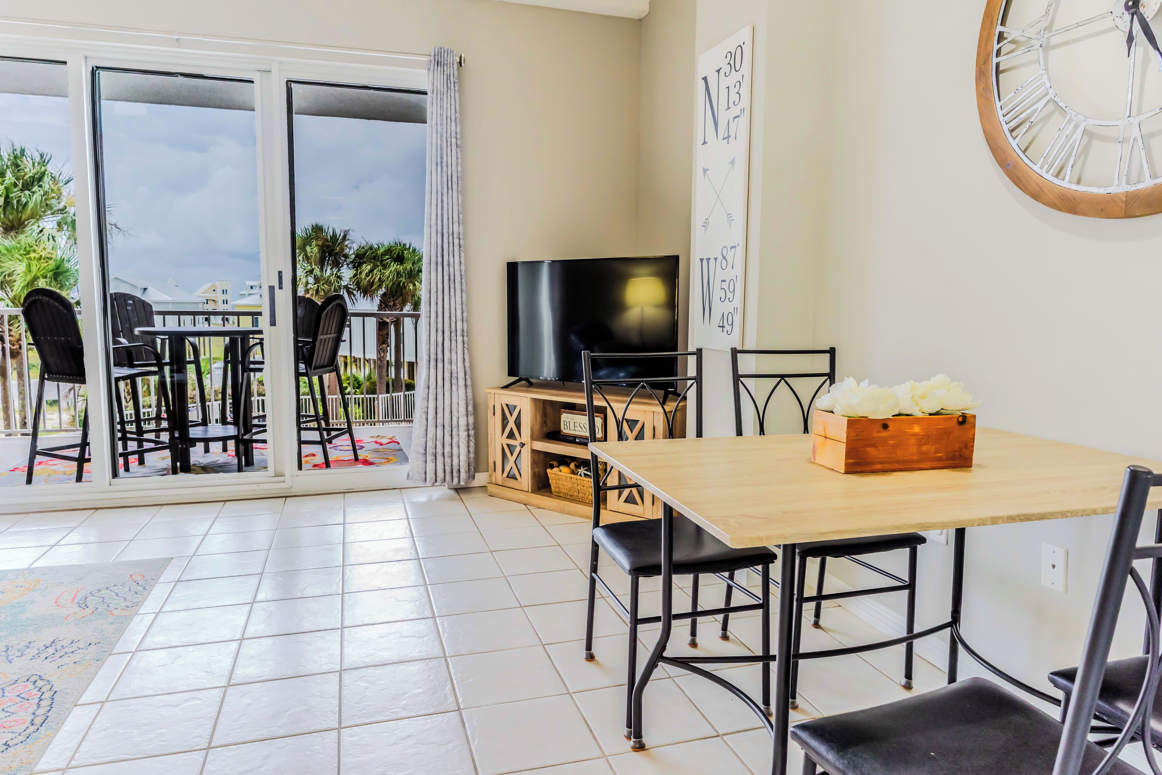 A dining area with a wooden table and chairs, a television, and a wall clock.