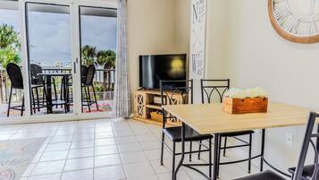 A dining area with a wooden table and chairs, a television, and a wall clock.