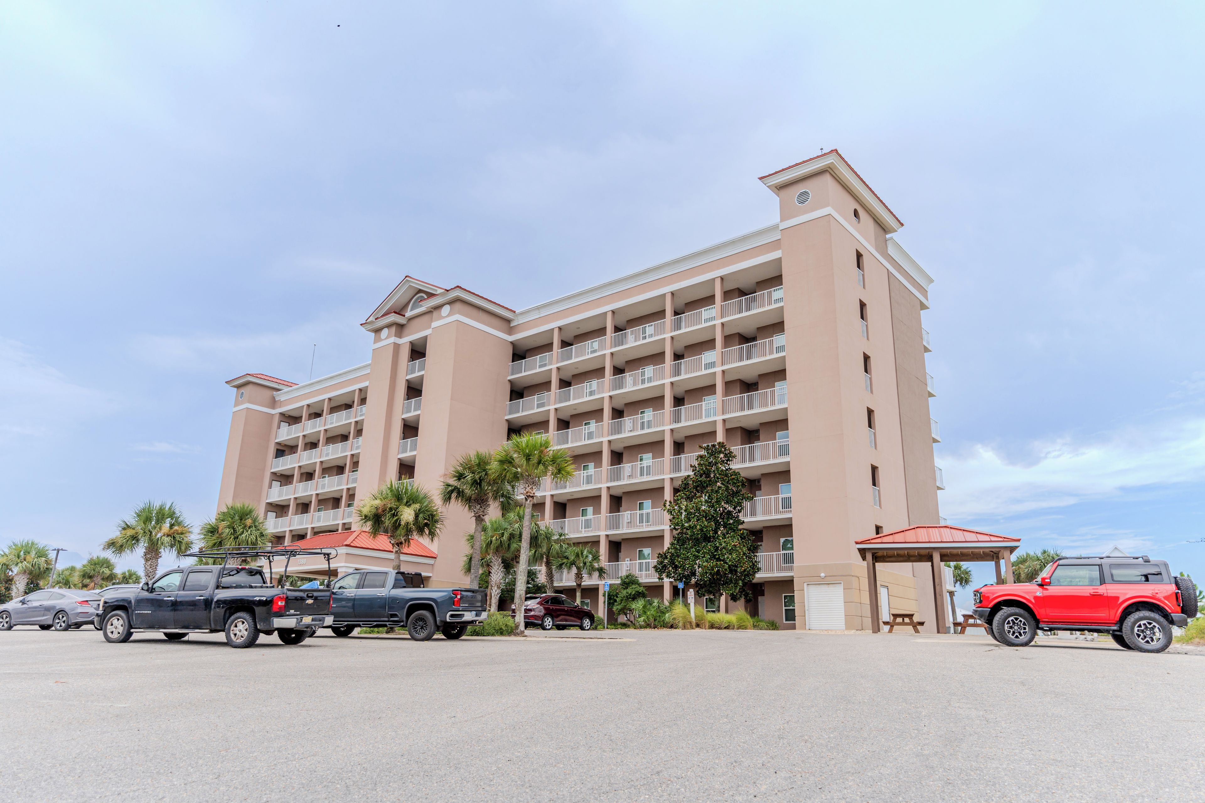 A multi-story hotel with a uniform facade, balconies, and a parking area with several vehicles.