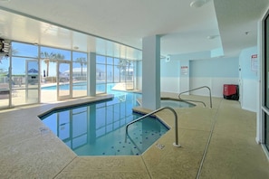 An indoor swimming pool with clear glass walls, a tiled floor, and a red fire extinguisher on the right.