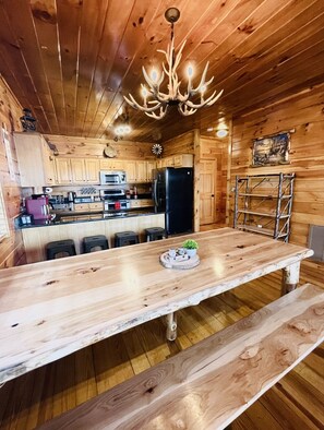 A wooden cabin interior with a central island table, a black refrigerator, and a chandelier.