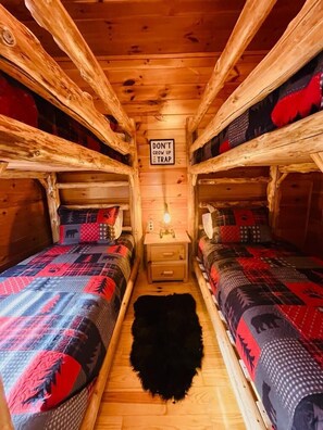 A cabin with two beds, a sign that says "DON'T GROW UP E TRAP", and a small nightstand with a lamp.