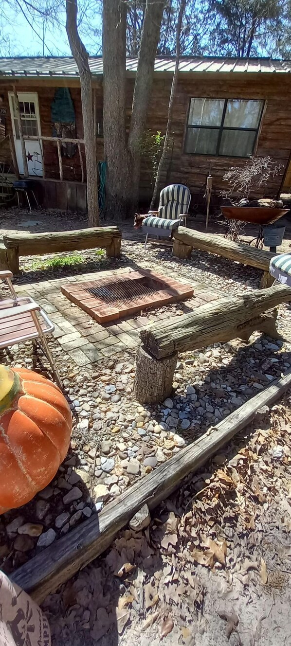 A rustic outdoor area with a wooden bench, a metal grill, and a large pumpkin decoration.