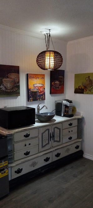 A kitchen with a white cabinet, a black microwave, a sink, and a coffee maker. There are three framed pictures on the wall. - ADORABLE BOHO CABIN JUST RENOVATED & ONLY 2 MILES TO TRADE DAYS (Canton)