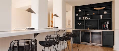 A modern kitchen with a white countertop, black bar stools, and a black shelving unit with kitchenware.