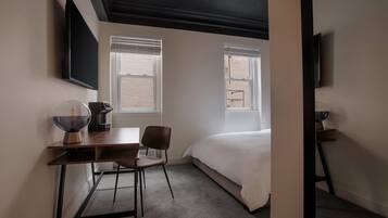 A hotel room with a bed, a desk with a chair, a coffee maker, and a TV mounted on the wall.