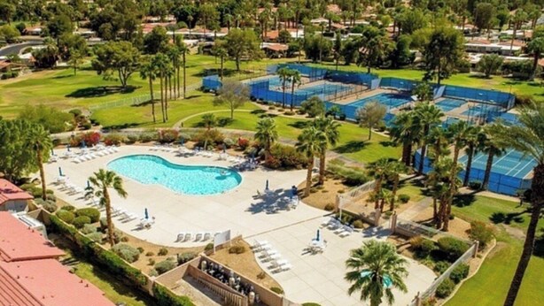 Ett semesterhotell med en stor pool, tennisbanor och palmer.