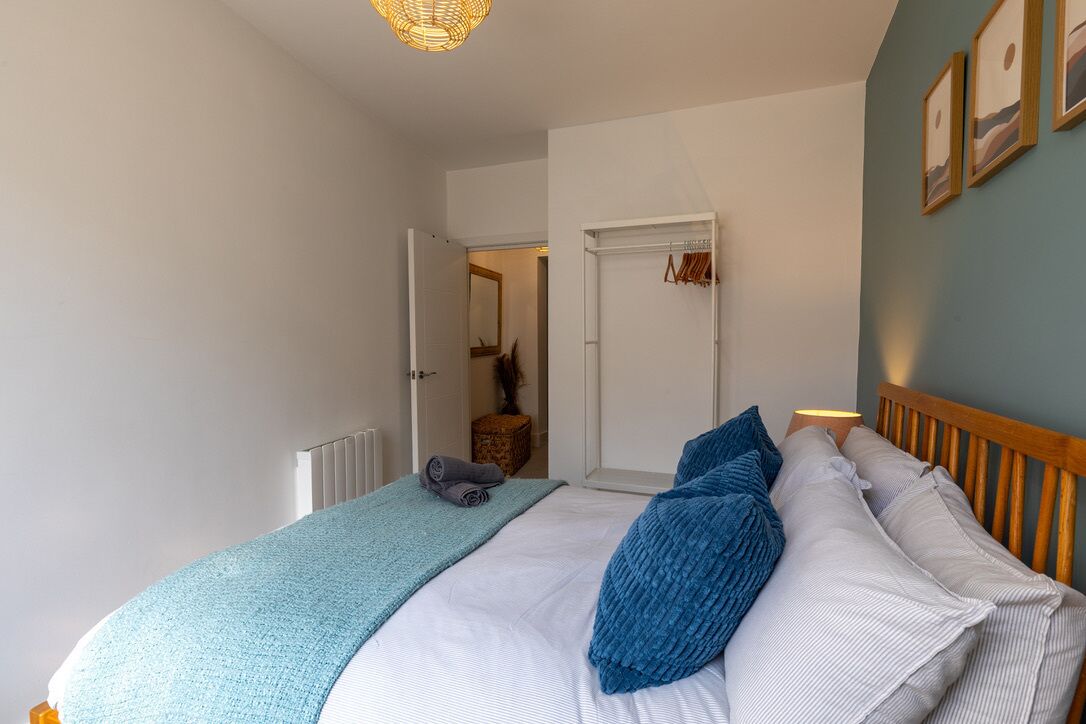 Un dormitorio con cama, mesita de noche, lámpara, puerta y una pared con cuadros.