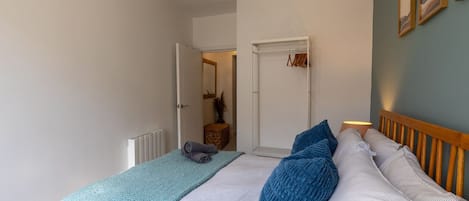 A bedroom with a bed, a bedside table, a lamp, a door, and a wall with framed pictures.