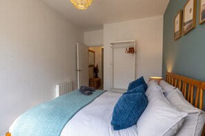 A bedroom with a bed, a bedside table, a lamp, a door, and a wall with framed pictures. - Courtyard Retreat (Southampton)