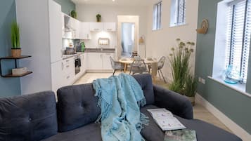 Un salon moderne comprenant un canapé, une table à manger avec des chaises, un coin cuisine et une fenêtre avec des stores.