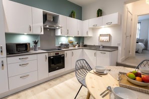 A modern kitchen with white cabinets, a microwave, and a dining area with a table set for two. - Courtyard Retreat (Southampton)