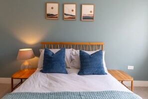 A bed with a wooden headboard, two pillows, a bedside lamp, and a small wooden table. - Courtyard Retreat (Southampton)