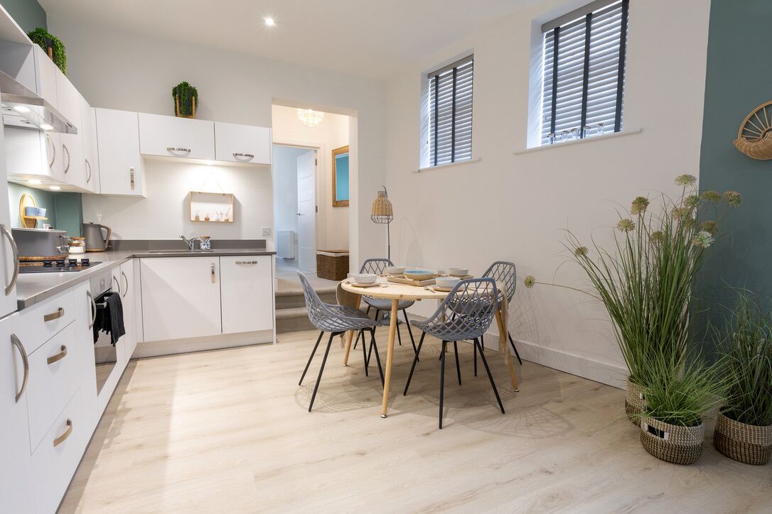 Una cocina moderna con armarios blancos, una mesa de comedor con sillas y plantas en macetas.