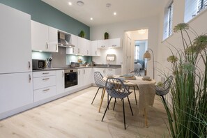 A modern kitchen with white cabinets, a dining area with a table and chairs, and a view into the living room. - Courtyard Retreat (Southampton)