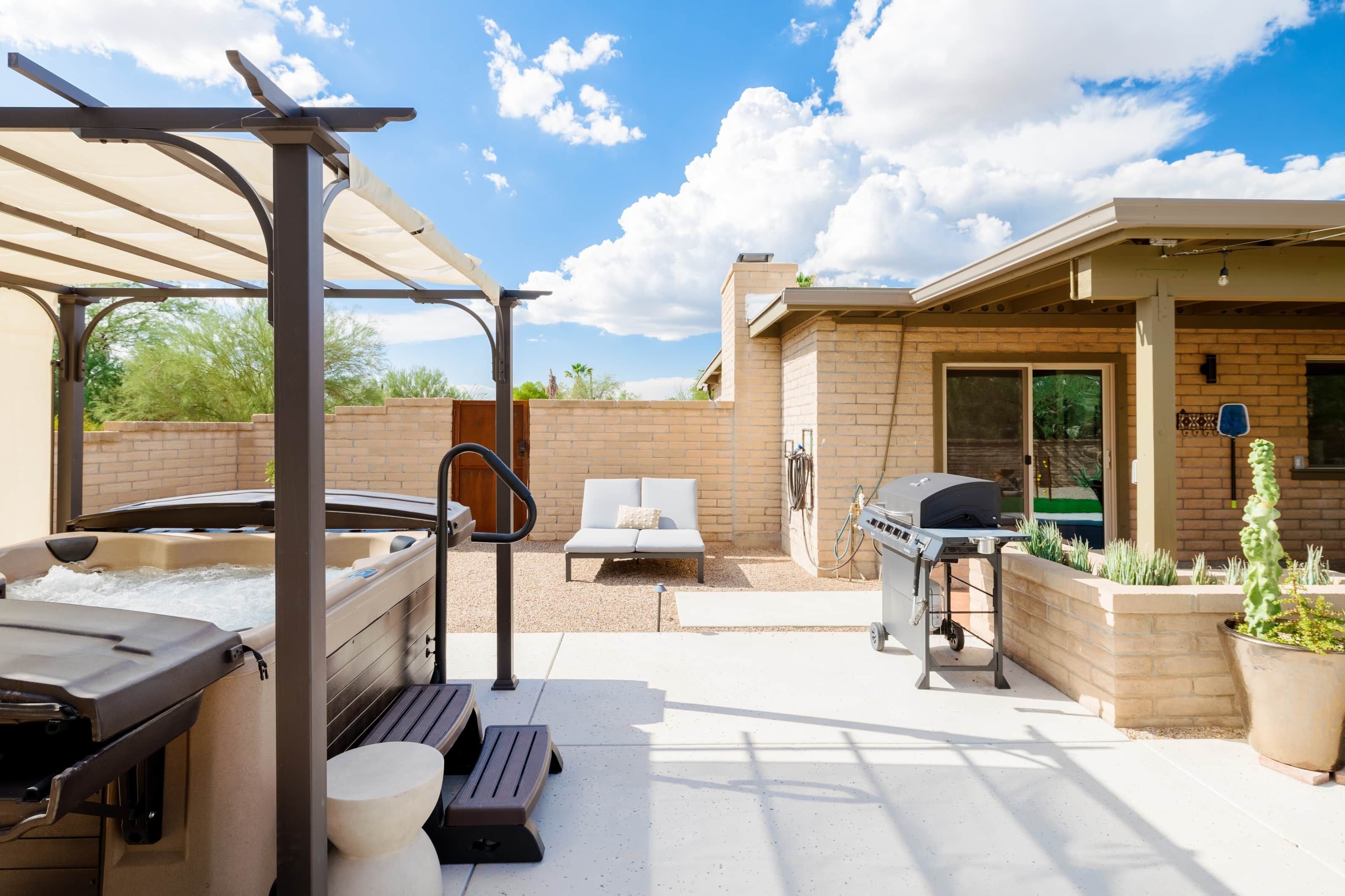 En udendørs terrasse med et spabad, liggestole, grill og en pergola.