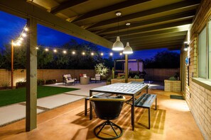 Un patio al aire libre con mesa y sillas, luces colgantes y una pared de ladrillo.