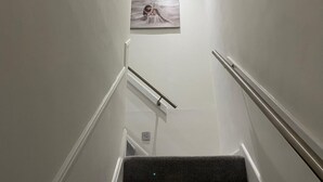 En smal trappa med ett ledstång på båda sidor, som leder upp till en liten plattform där ett inramat konstverk hänger.