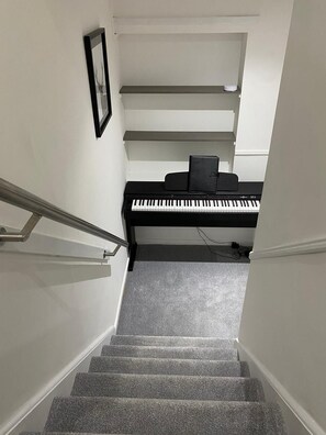 Una escalera conduce a un piano en una habitación con paredes blancas y piso alfombrado.