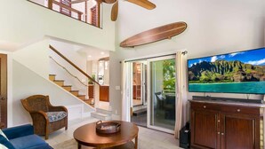 Amplia sala de estar con una escalera, televisor y vistas a un paisaje tropical.