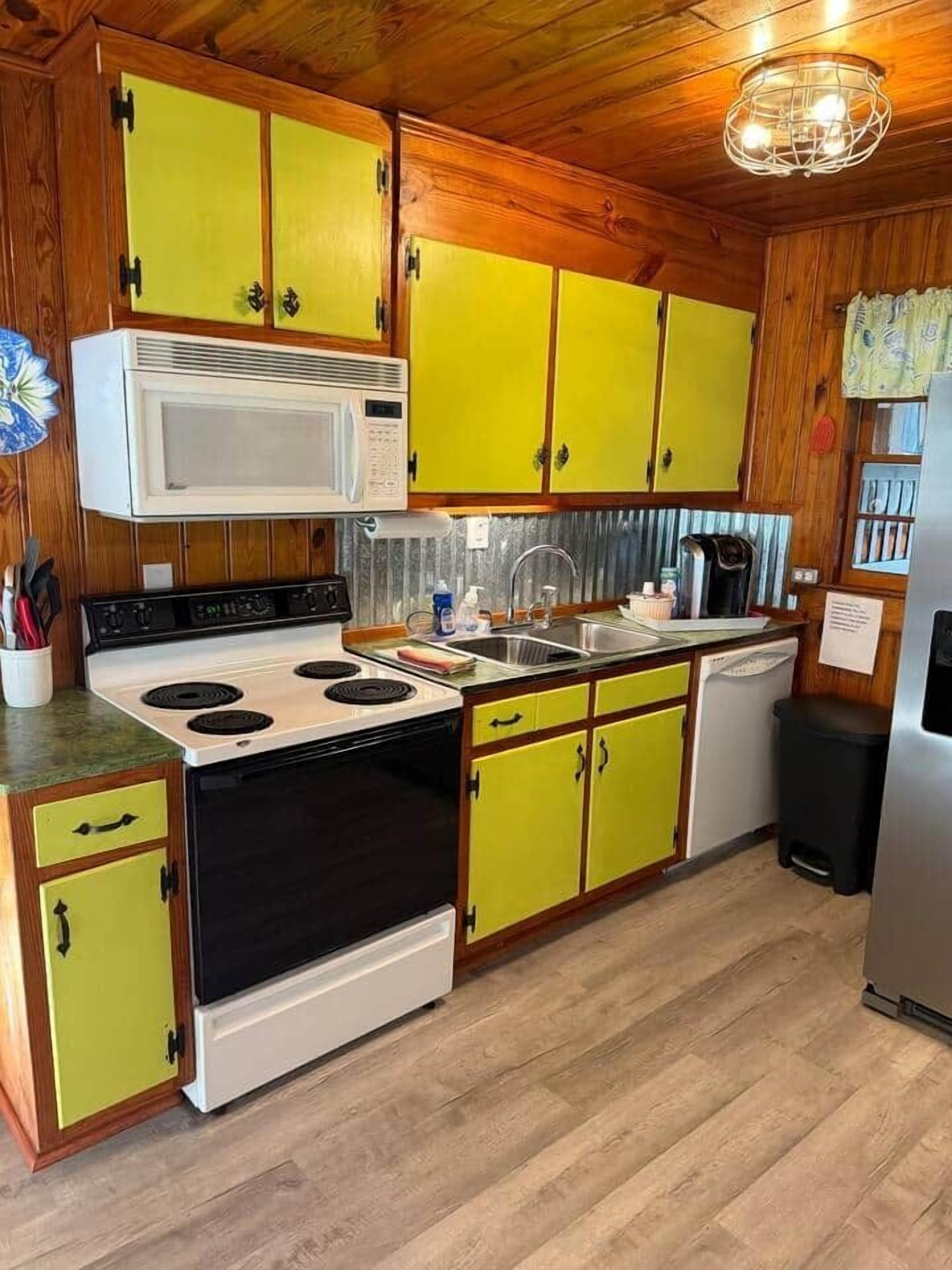 Una cocina con gabinetes de madera, estufa, microondas y pileta.
