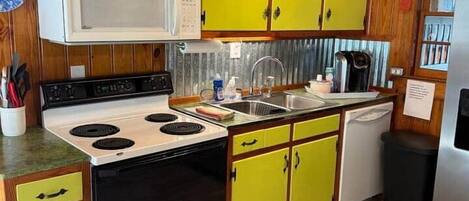 Una cocina con gabinetes de madera, estufa, microondas y pileta.