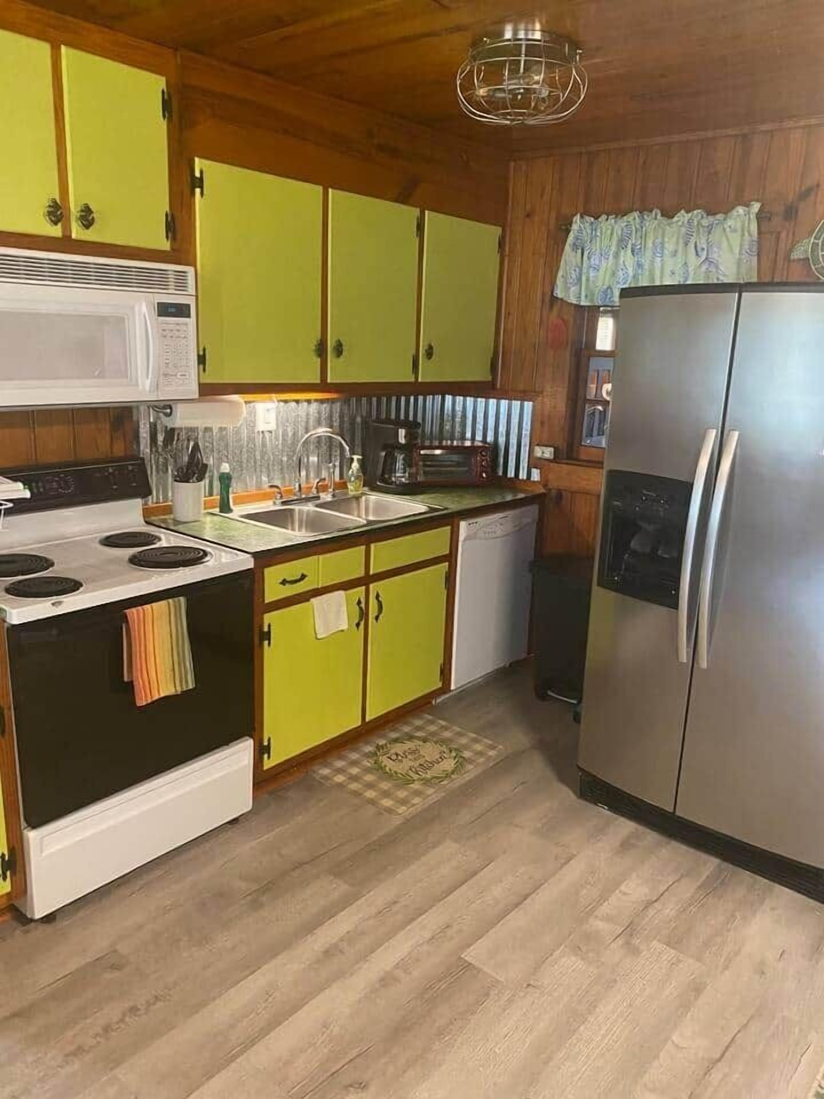 Une cuisine avec des meubles de rangement en bois, une cuisinière, un four à micro-ondes, un évier et un réfrigérateur.