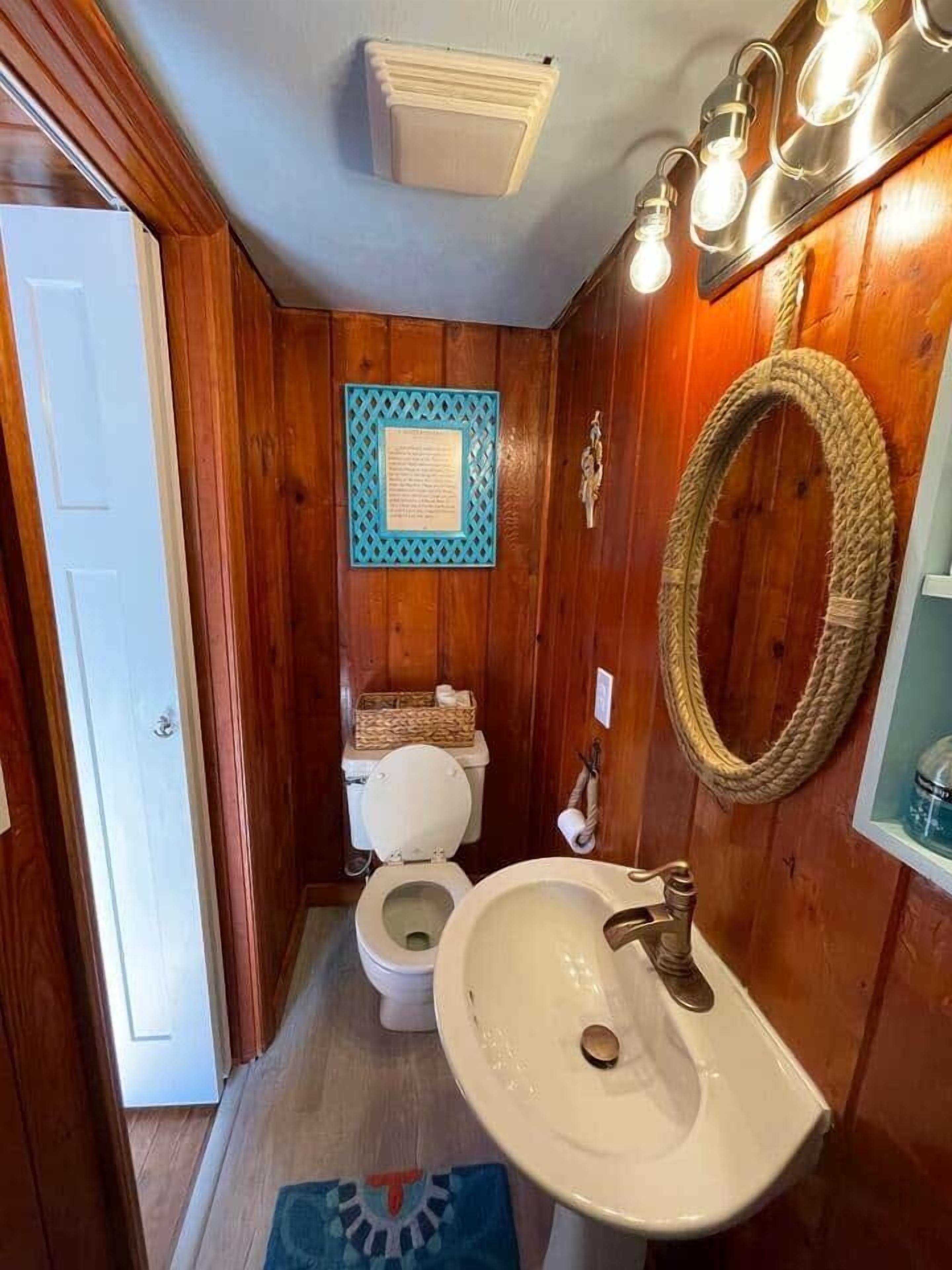 A wooden-paneled bathroom with a toilet, sink, and a wall-mounted mirror.