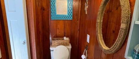 A wooden-paneled bathroom with a toilet, sink, and a wall-mounted mirror.