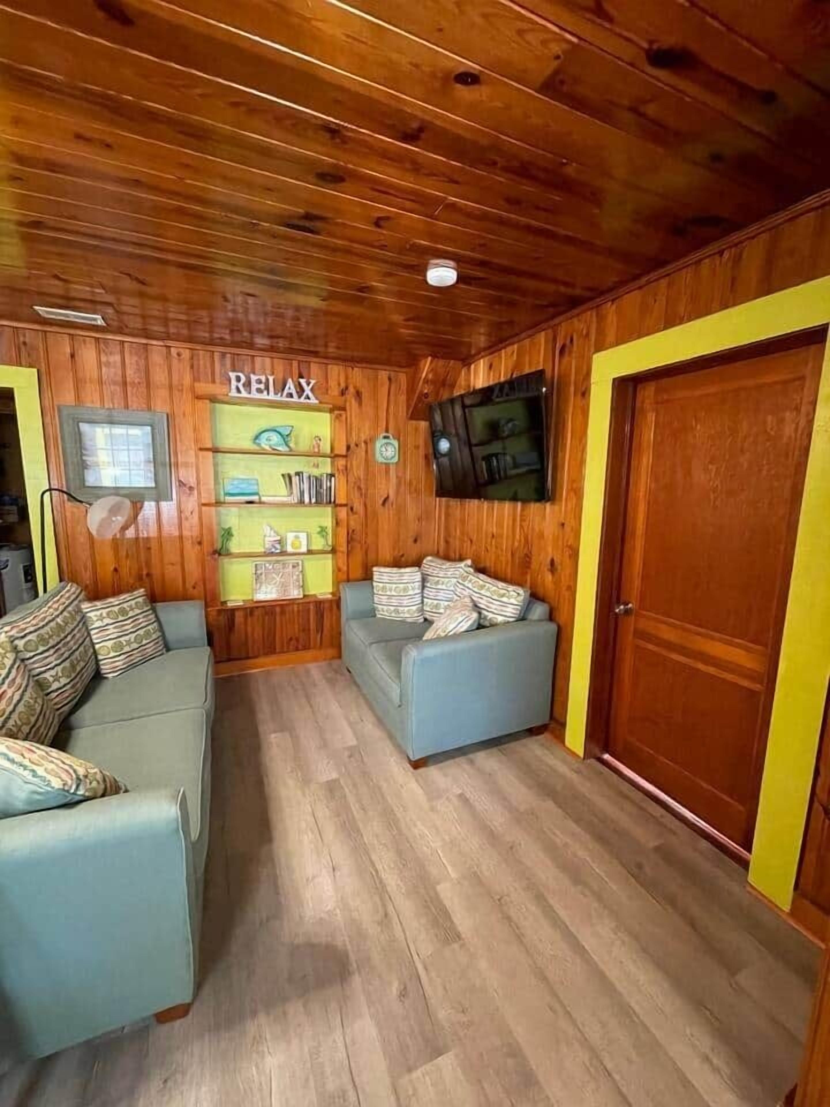 A cozy room with wooden walls, a blue sofa, a bookshelf, and a TV mounted on the wall.