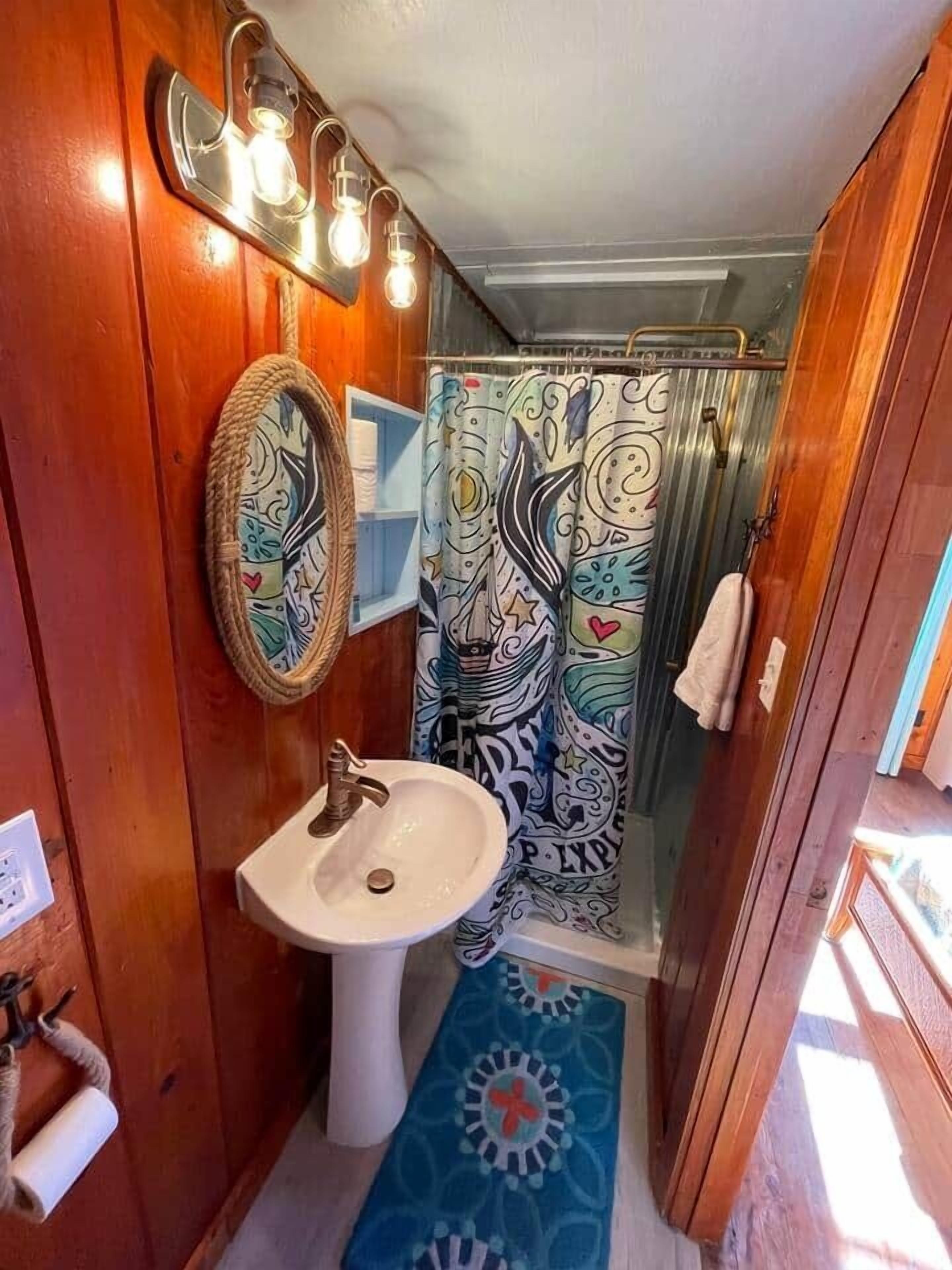 Ein kleines Badezimmer mit einem weißen Waschbecken, einem Spiegel und einer Duschtasse mit buntem Muster.