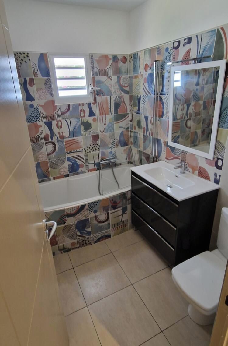 Une salle de bain avec une baignoire, un lavabo et des toilettes. Les murs sont recouverts de carreaux formant un motif abstrait et coloré.