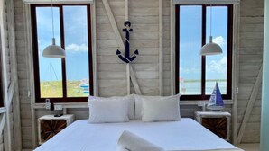Quarto com uma cama grande, duas mesas de cabeceira e vista para o mar através de duas janelas.