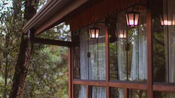 A wooden cabin with large windows and hanging lanterns, surrounded by dense forest.