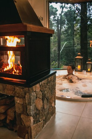 Ein Steinkamin mit sichtbarem Feuer, eine Steinwand und eine Hot Tub, in der eine Person sitzt.