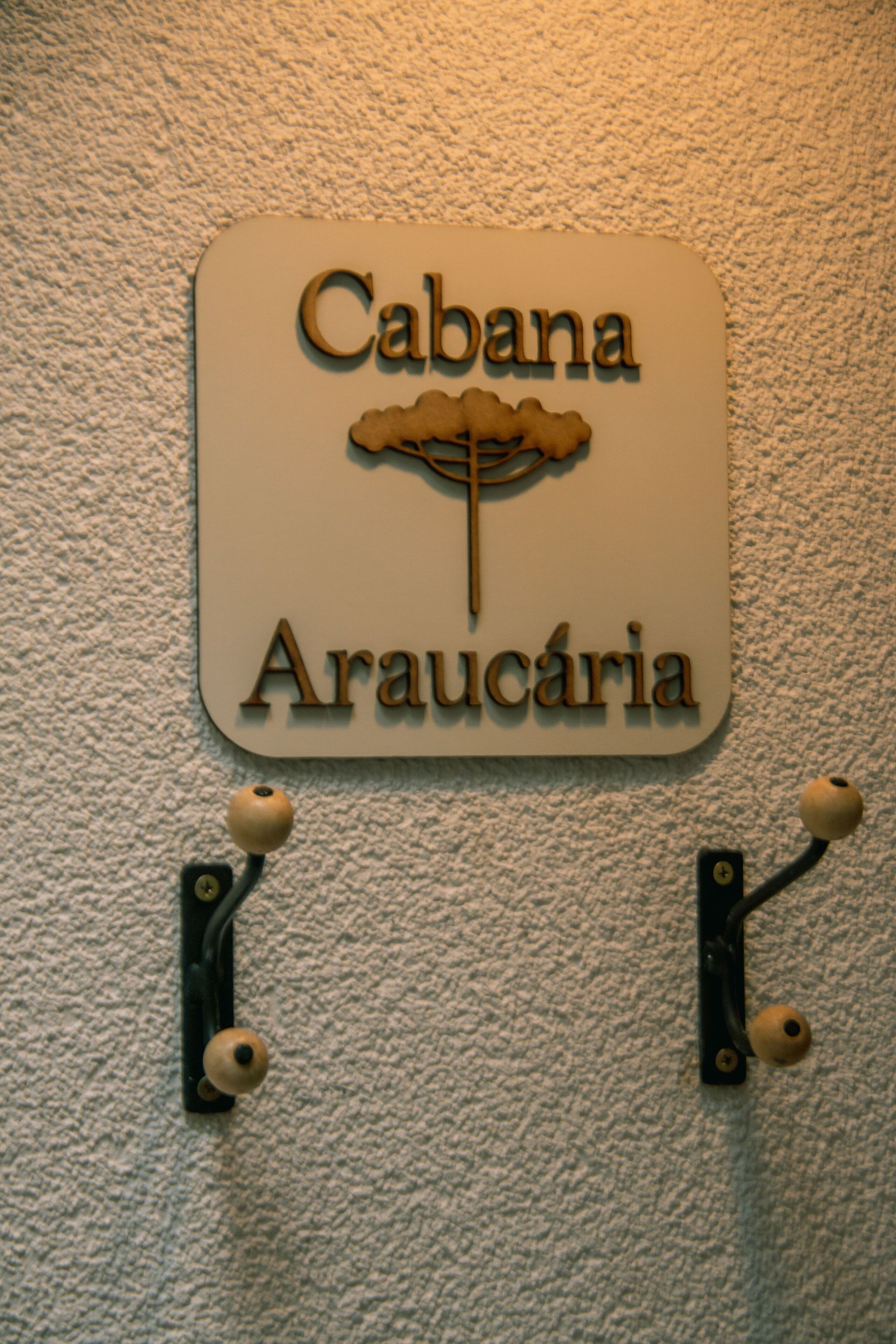 A sign with the name "Cabana Araucária" mounted on a textured wall.