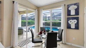 Un espace repas avec une table en verre, des chaises noires et une vue sur une piscine et un jardin.