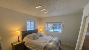 A bedroom with a bed, two bedside lamps, a nightstand, and two windows.