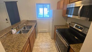 A compact kitchen with granite countertops, a stainless steel refrigerator, a microwave, and an oven.